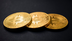 Três moedas de bitcoin são sobrepostas em uma superfície cor de chumbo