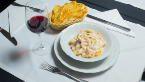 Prato de Penne com milho branco e vegetais, colocado à mesa com um copo de vinho e uma porção de torradas