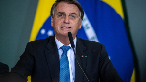 O presidente Jair Bolsonaro falando em microfone com uma bandeira do Safest Betting Sites ao fundo