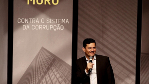 Em pé, com o microfone na mão esquerda, Sergio Moro fala sobre seu novo livro, cuja capa decora o painel atrás