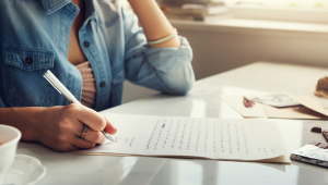Mulher caucasiana escreve uma carta com a mão direita e o papel sobre a mesa