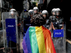 Manifestante aparentemente do sexo feminino, com bandeira do arco-íris amarrada nas costas, encara polícais em rua de Istambul