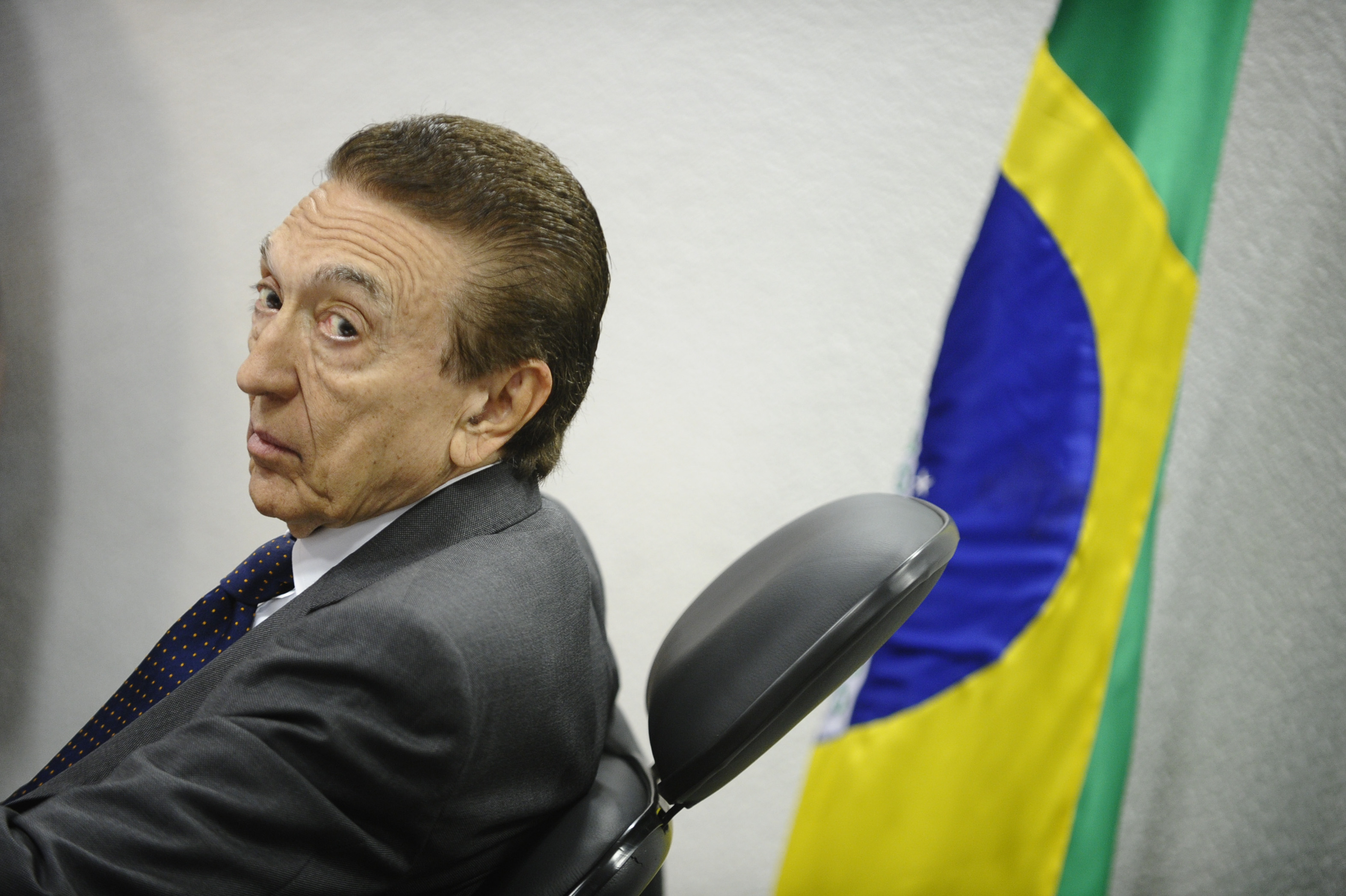 Edison Lobão sentado em frente a bandeira do Brasil
