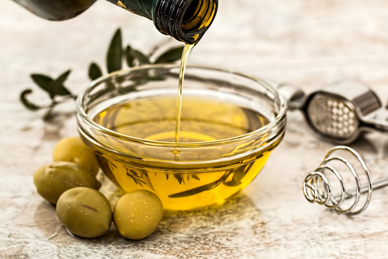 Imagem de um pote de vidro com azeite de oliva e três azeitonas ao lado