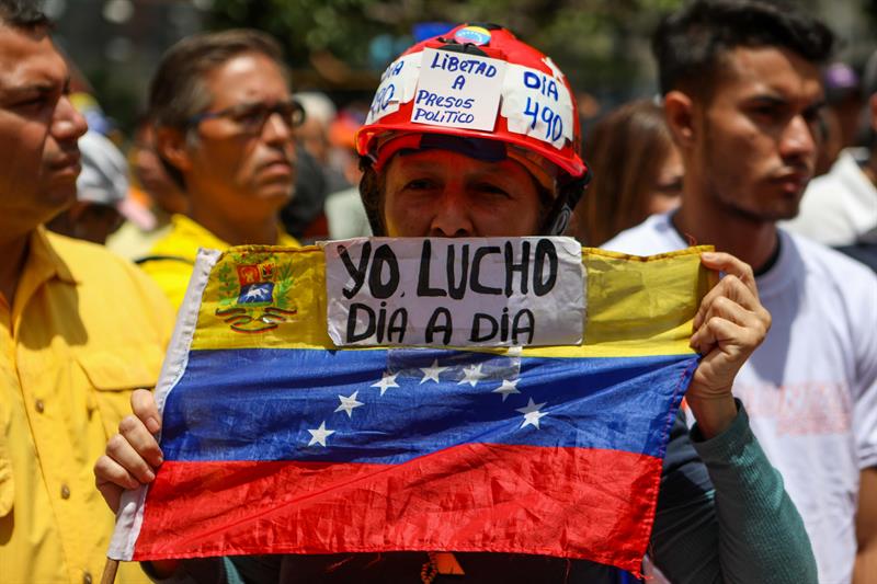Pessoa segurando uma bandeira da Venezuela escrito em espanhol 