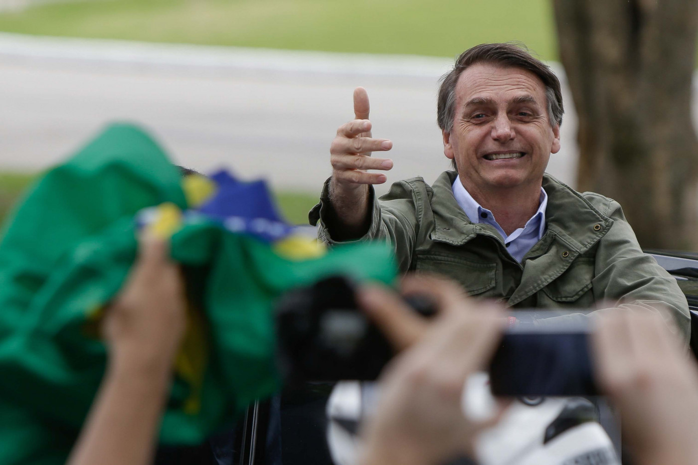 Jair Bolsonaro fazendo sinal de positivo com câmeras e bandeiras do Brasil