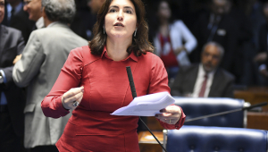 Senadora Simone Tebet segurando um papel e falando em sessão na Câmara. Usa blusa vermelha de mangas compridas e tem cabelos na altura do ombro castanhos