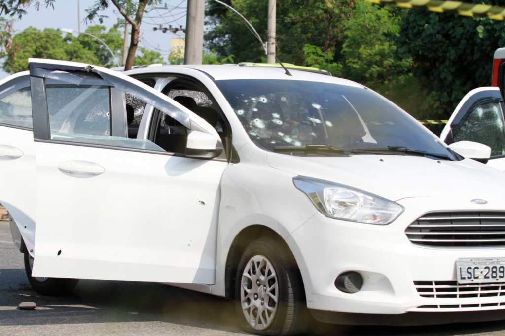 Carro branco com porta aberta e diversas marcas de tiros