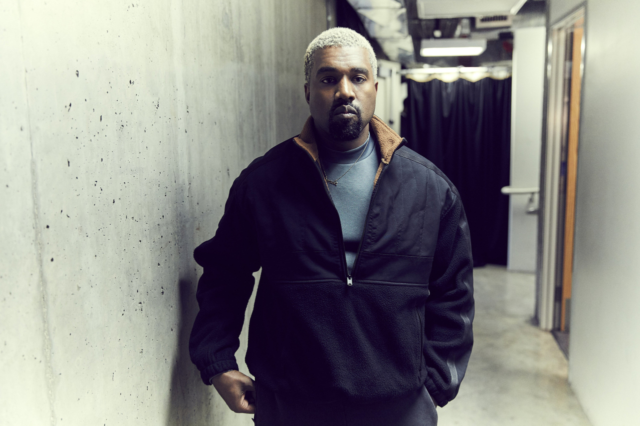 Kanye West encostado em parede cinza