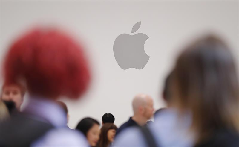 Pessoas cmainham em frente ao logotipo da Apple, uma maçã mordida