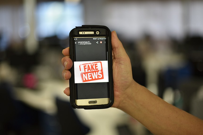 Um celular na mão de uma pessoa com uma imagem escrito 'Fake News'