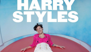 Homem deitado embaixo de letreiro com os dizeres Harry Styles