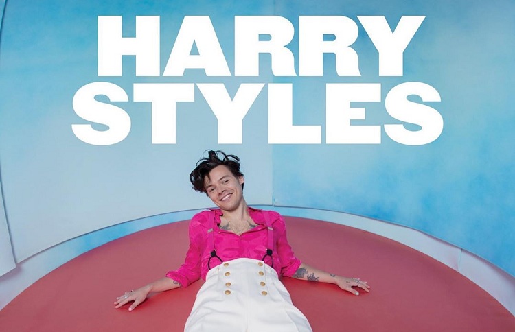 Homem deitado embaixo de letreiro com os dizeres Harry Styles