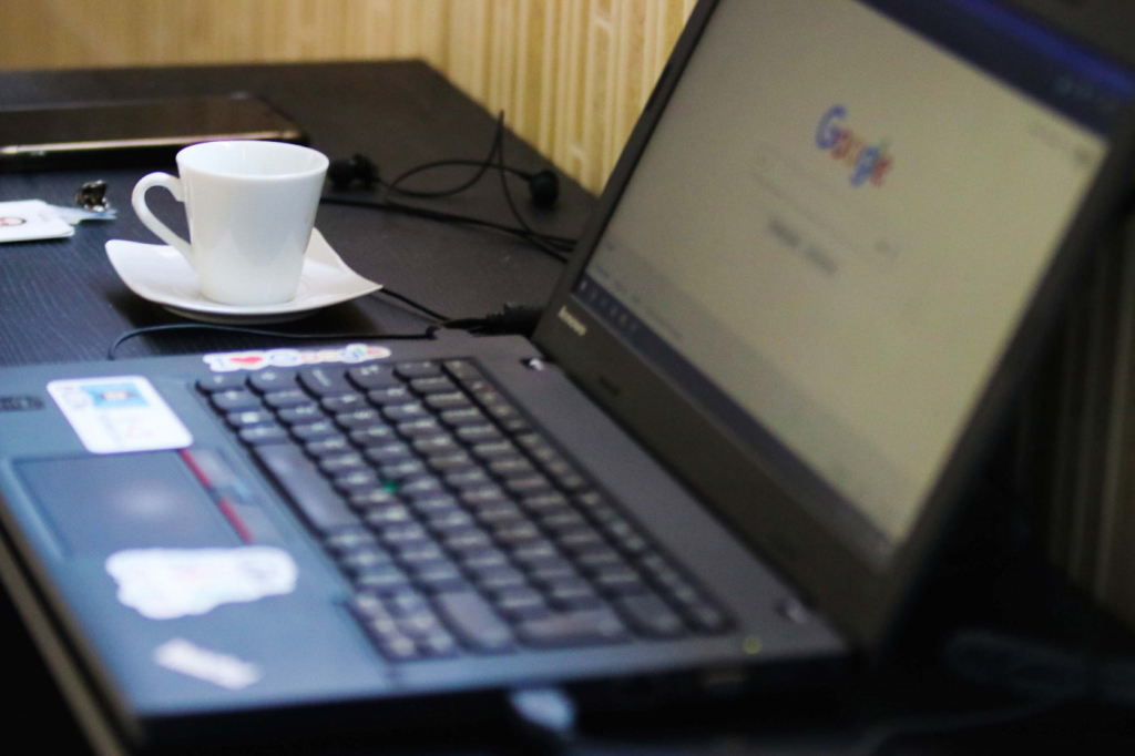 notebook aberto com xícara branca de café ao longo. página do google no desktop