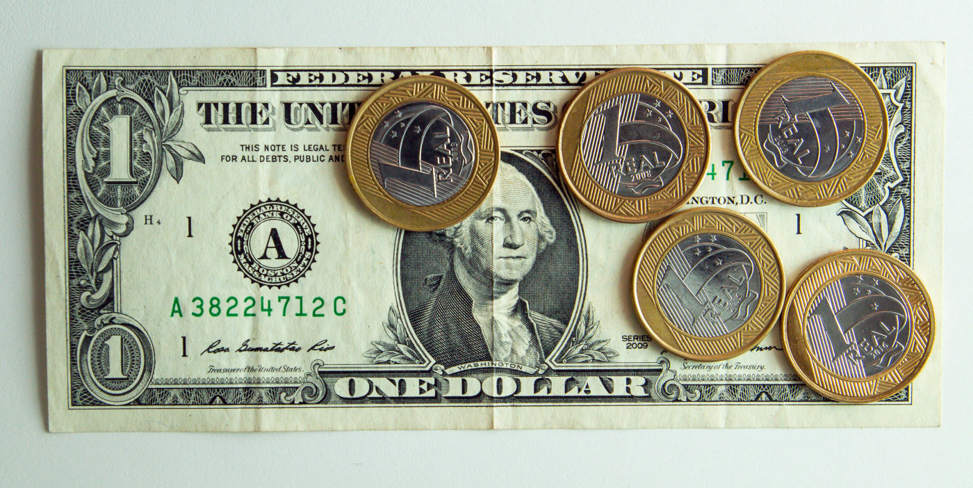 Nota de dólar embaixo de cinco moedas de real