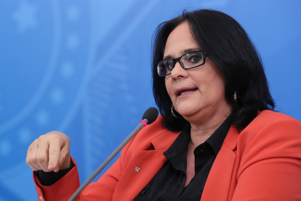 ministra damares alves. mulher branca de cabelo chanel preto, falando ao microfone, com casaco vermelho