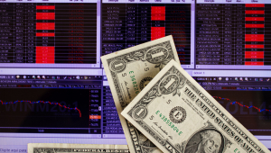 Notas de dólar em frente a painel que mostra variações de ações da Bolsa