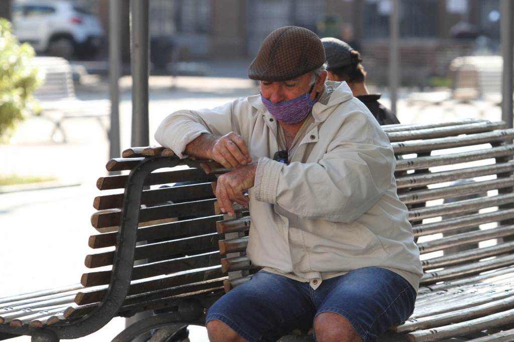 Idoso sentado em banco de uma praça usando máscara de proteção