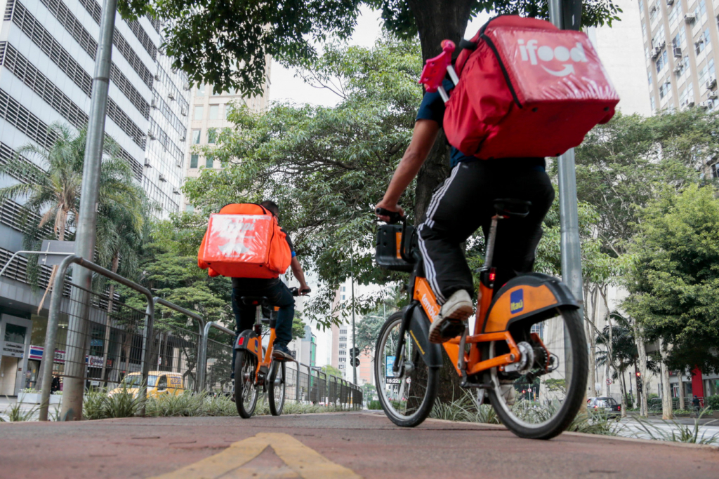 entregadores de aplicativo em cima de bicicletas laranjas do Itaú