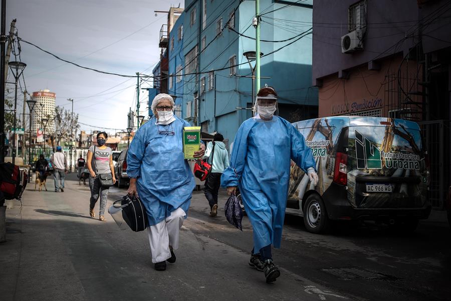duas pessoas caminhando em uma cidade com uniformes azuis e máscaras face-shield