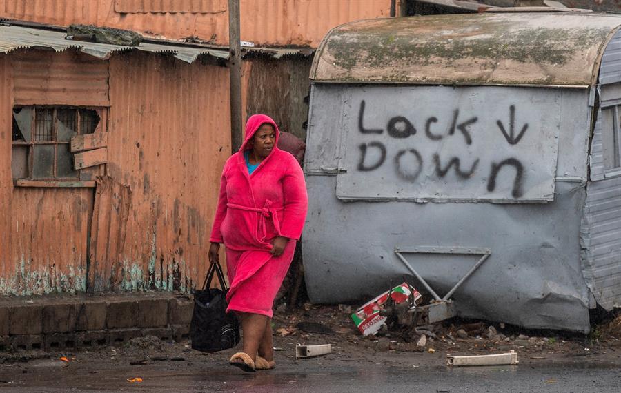 Mulher vestida de rosa caminhando em uma rua com aspecto sujo e a palavra lock down escrita na caçamba