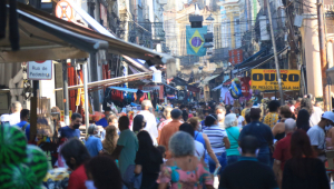 Pessoas caminhando em uma rua cheia com uma bandeira do Brasil atrás