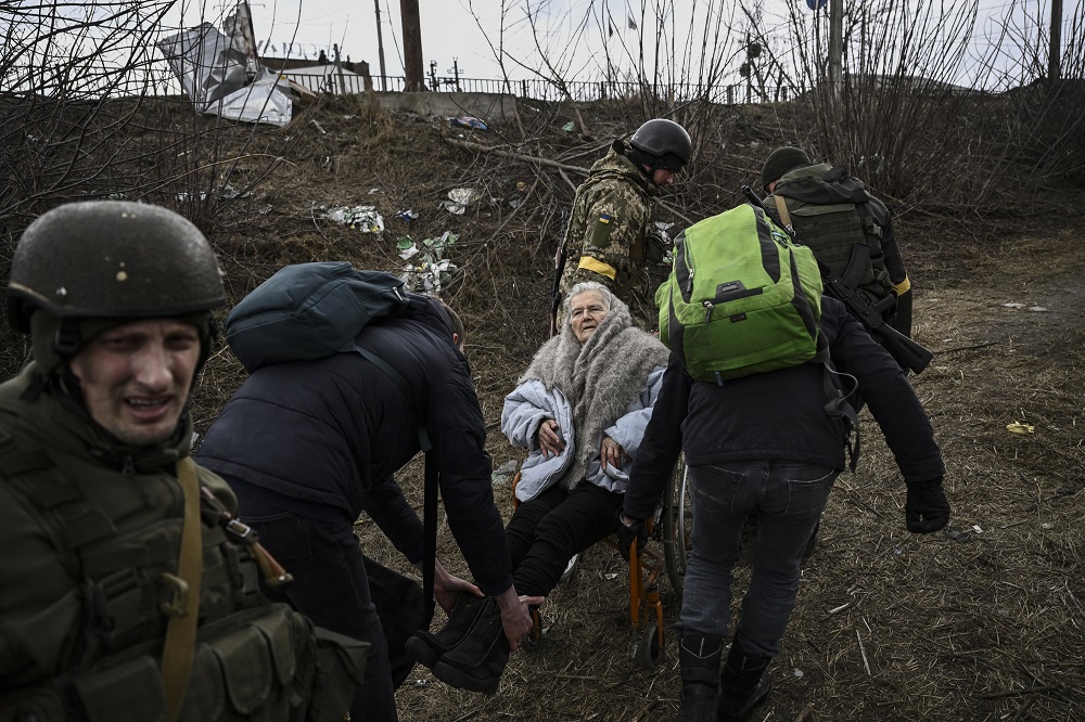 Pessoas ajudam uma idosa em cadeira de rodas enquanto fogem da cidade de Irpin, a oeste de Kiev, em 7 de março de 2022. na capital Kiev, pois civis aterrorizados não conseguiram escapar pelo segundo dia de Mariupol sitiada