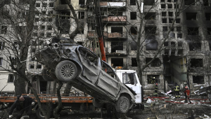 Um guindaste remove um carro arruinado da frente de um prédio de apartamentos destruído depois de ter sido bombardeado no distrito de Obolon, no noroeste de Kiev