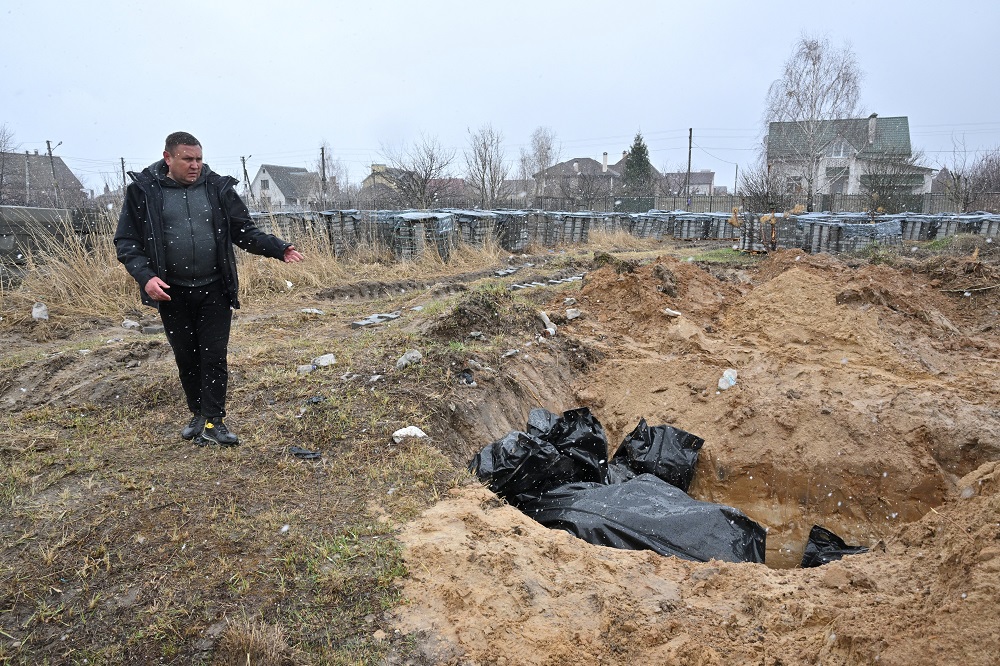 Homem gesticula para uma vala comum na cidade de Bucha, a noroeste da capital ucraniana, Kiev