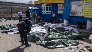 policial ucraniano se curva sobre corpos deitados no chão e cobertos com lona depois que um ataque com foguete em estação de trem em Kramatorsk