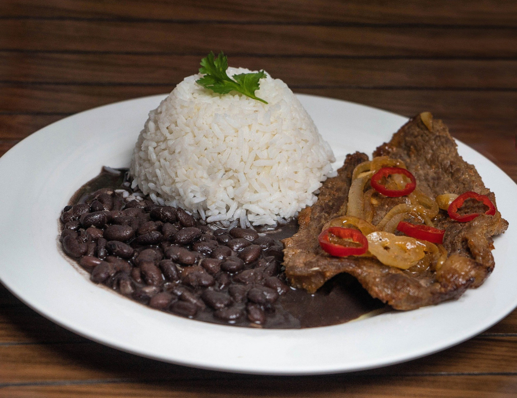 Prato branco com feijão preto, bife e arroz