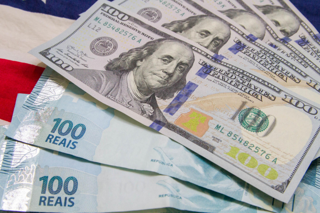 Notas de real e dólar espalhadas em cima de uma bandeira dos Estados Unidos