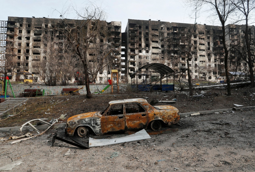Carro queimado em frente a prédios residenciais destruídos durante conflito Ucrânia-Rússia na cidade sitiada de Mariupol, na Ucrânia