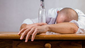 Homem com garrafa se debruça sobre uma mesa