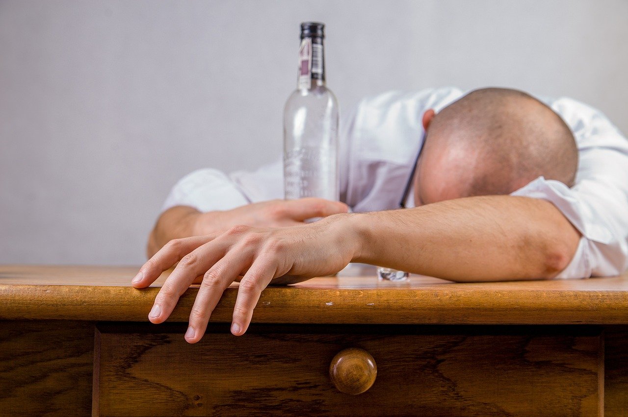 Homem com garrafa se debruça sobre uma mesa