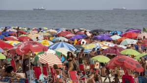 Aglomeração de pessoas e sombrinhas de sol na frente da praia