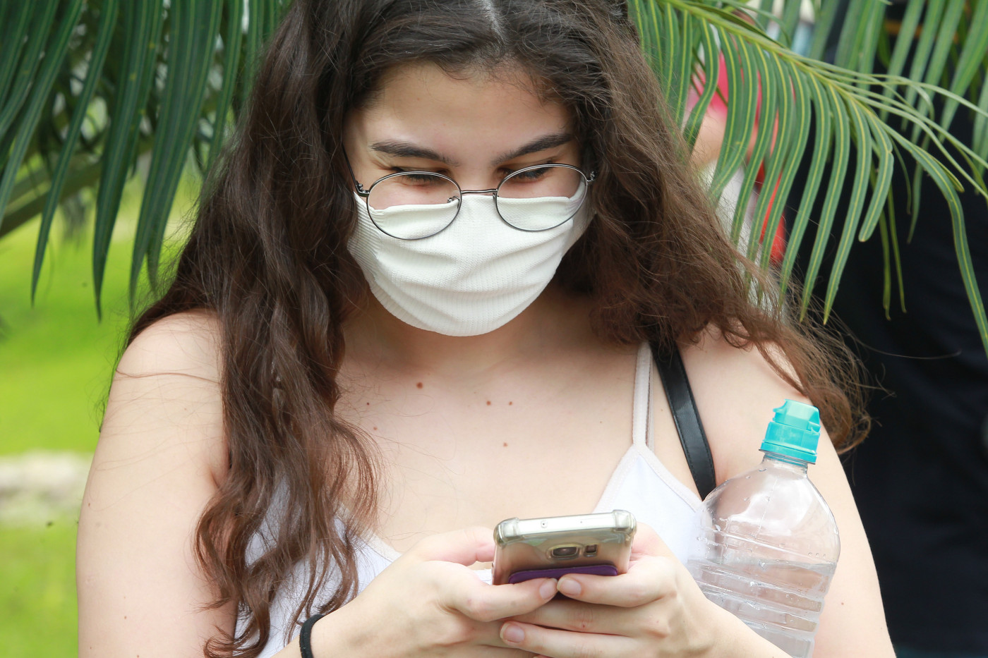Estudante usando máscara e mexendo no celular após término do vestibular