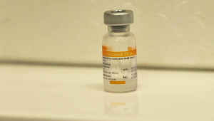 Frasco de vacina com rótulo laranja e branco na frente de um fundo branco