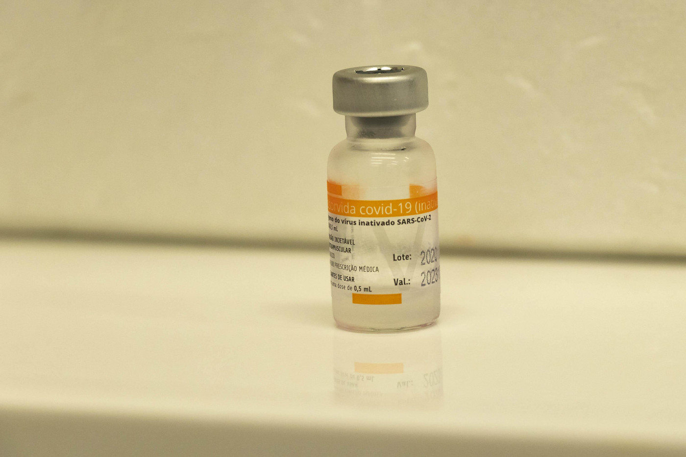 Frasco de vacina com rótulo laranja e branco na frente de um fundo branco