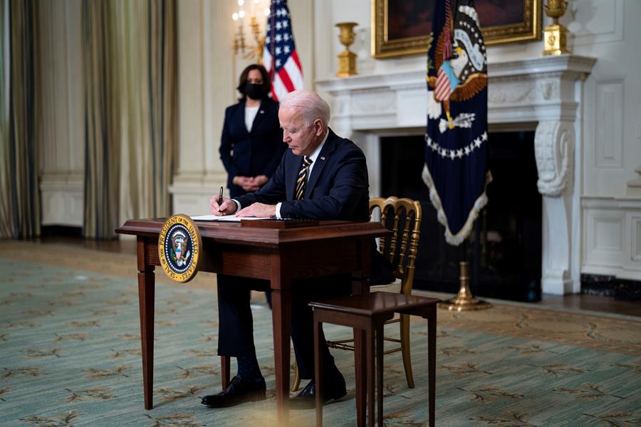 Presidente dos Estados Unidos, Joe Biden, assina decreto ao lado da bandeira nacional com a vice-presidente Kamala Harris ao fundo