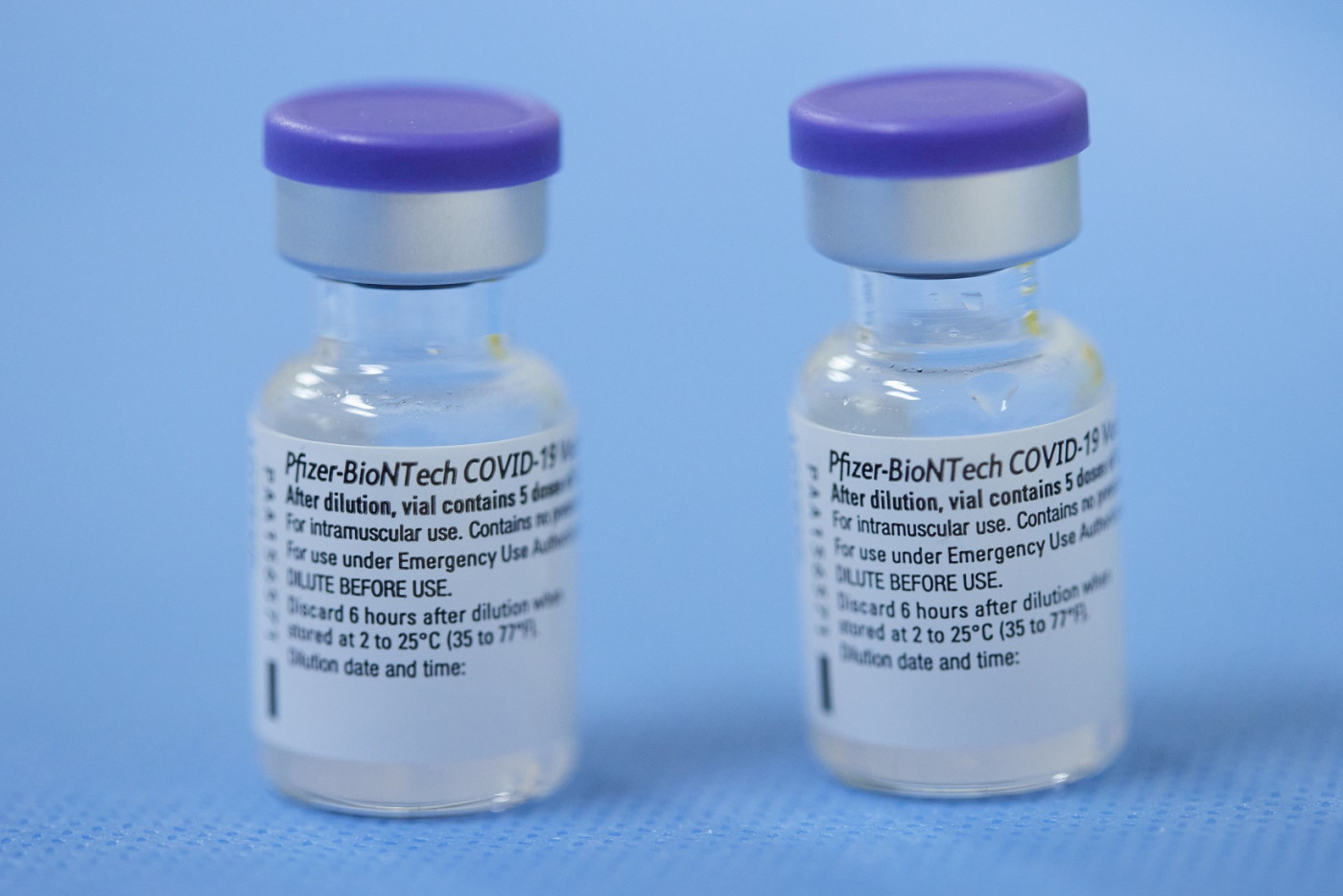 Dois frascos de vacina com tampa roxa diante de um fundo azul