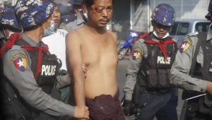 Manifestante com olho machucado é levado por policiais no Myanmar, que sofreu um golpe militar no dia 1 de fevereiro
