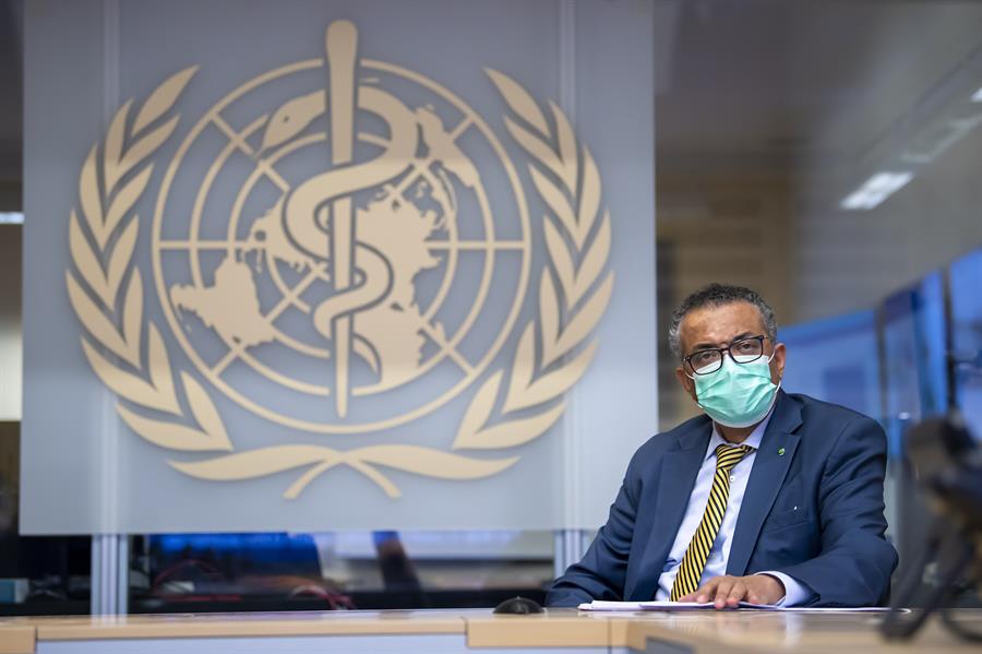 Usando máscara, o diretor-geral Tedros Adhanom posa em frente ao símbolo da Organização Mundial da Saúde