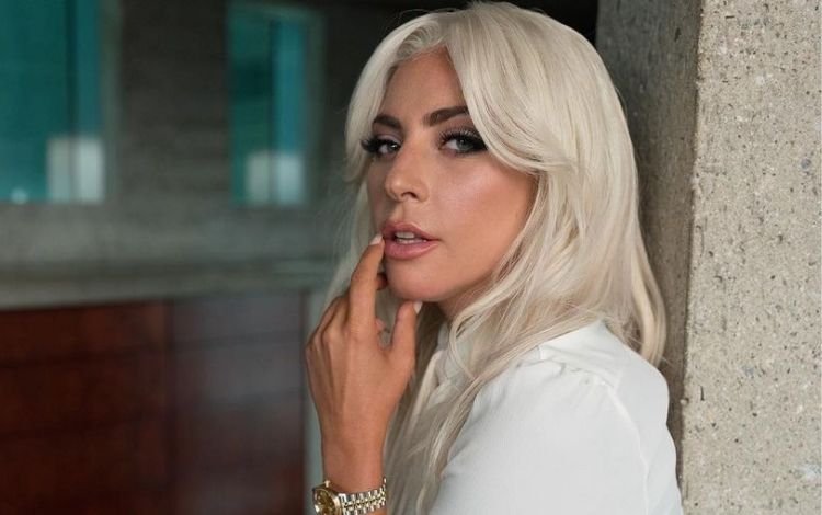 Lady Gaga com cabelo branco, dedo na boca e olhando para o lado. Foto de perfil, busto
