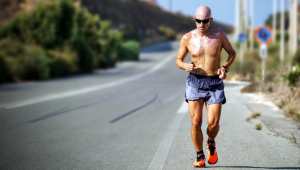 Homem careca correndo na pista sem blusa, de shorts e com óculos de sol
