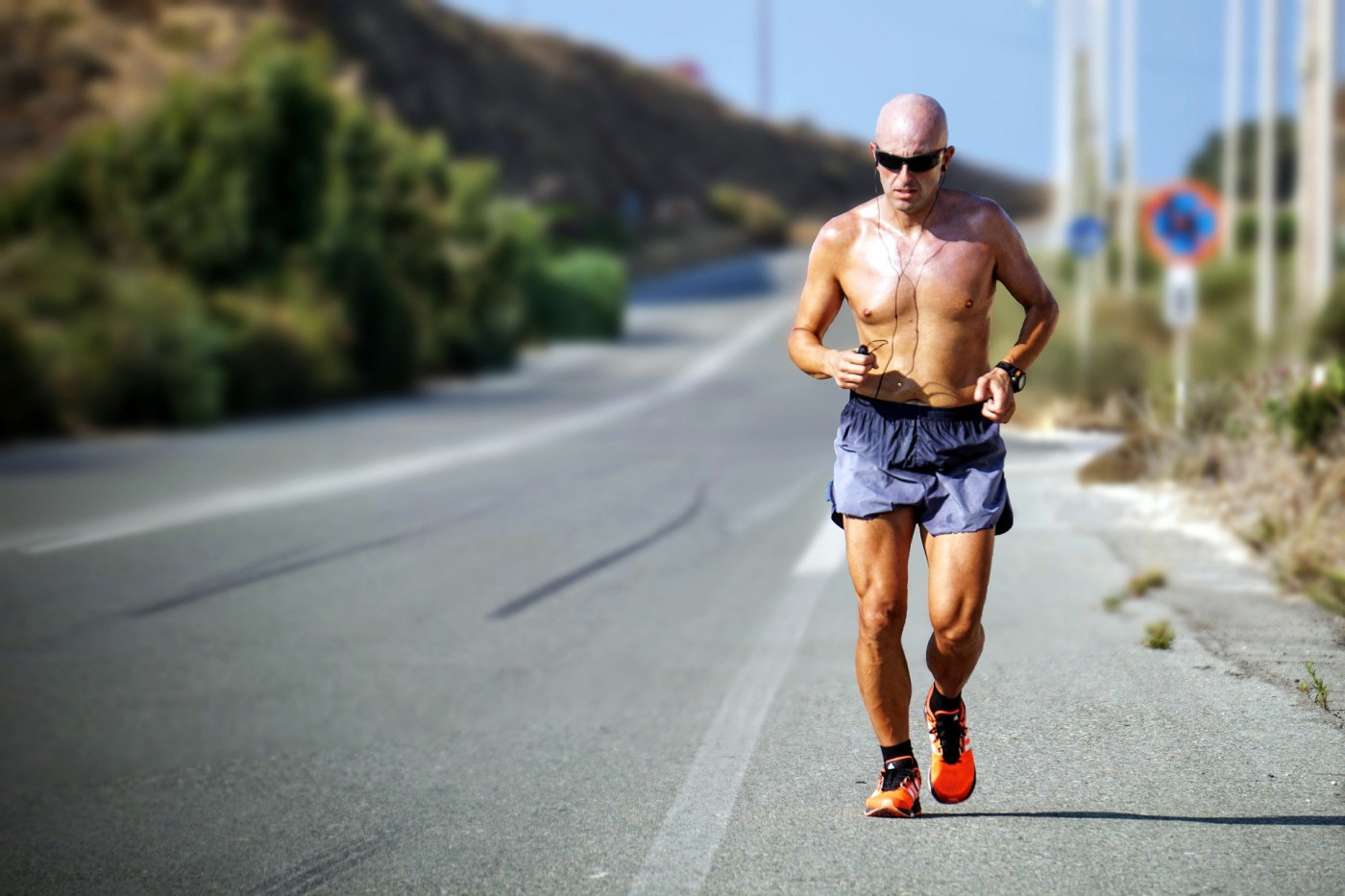 Homem careca correndo na pista sem blusa, de shorts e com óculos de sol