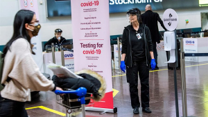 Funcionária do Aeroporto de Estocolmo, na Suécia, ao lado de placa que indica estação de testes de Covid-19