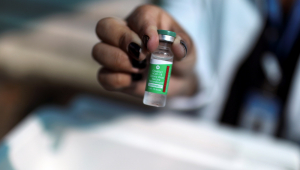 mão segurando frasco de vacina com rótulo verde em primeiro plano