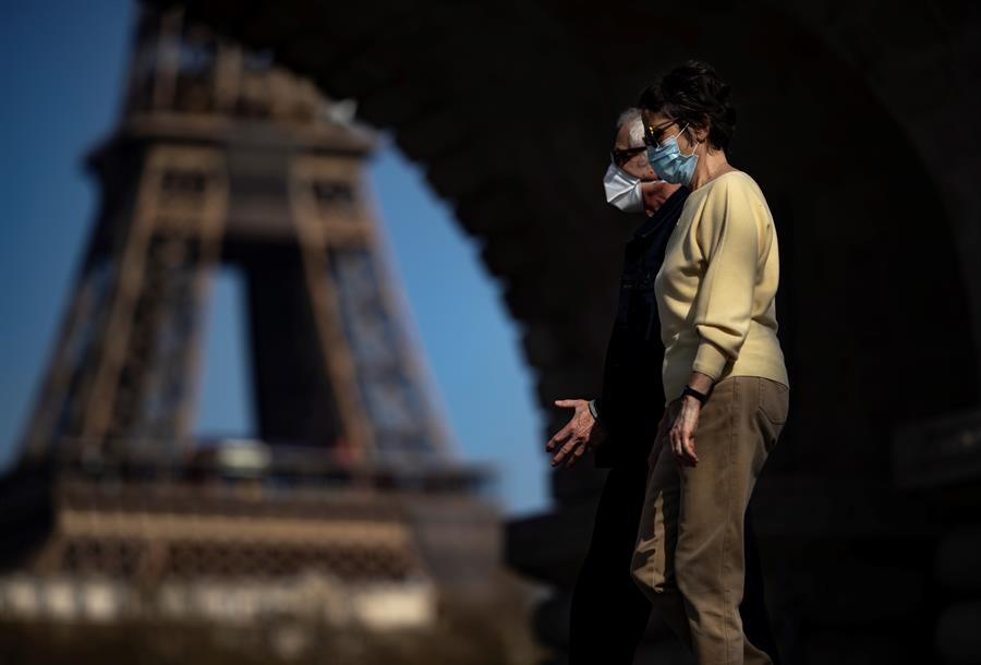 Pessoas usando máscaras passeiam em frente à Torre Eiffel em Paris, na França