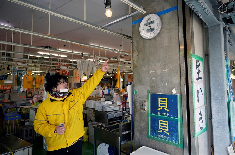 Funcionário de uma loja mostra o nível que a água atingiu em Fukushima durante o tsnumani do Japão em 2011